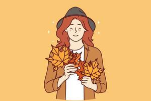 Woman with autumn leaves in hands smiles standing in stylish casual clothes and hat. Cheerful young girl rejoices at onset of autumn season and collects beautiful foliage from trees vector