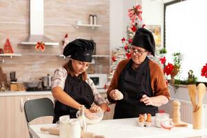 nieto preparando hecho en casa masa con abuela celebrando Navidad temporada juntos en Navidad decorado culinario cocina. niño disfrutando invierno fiesta Cocinando pan de jengibre postre foto