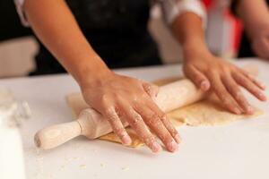 Closeup of granddaughter hands preparing homemade gingerbread using rolling pin making cookies dough celebrating christmas holiday. Child cooking delicious xmas dessert enjoying winter season photo