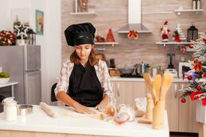 Child wearing baking apron putting flour on homemade dough preparing traditional gingerbread dessert enjoying winter holiday in xmas decorated kitchen. Kid celebrating christmas season making cookies photo