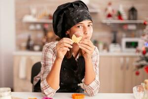 retrato de niño con delantal participación hecho en casa masa Cocinando pan de jengibre postre en Navidad culinario decorado cocina. nieto horneando tradicional postre a hogar celebrando Navidad fiesta foto