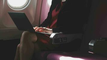 mujer joven asiática que usa una computadora portátil sentada cerca de las ventanas en primera clase en un avión durante el vuelo, los viajes y el concepto de negocios video