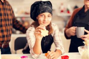 Grandchild on christmas day holding shaped pastery wearing apron and bonette. Happy cheerful joyfull teenage girl helping senior woman preparing sweet cookies to celebrate winter holidays. photo