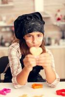 Grandchild looking at heart shaped pastry on christmas day wearing apron and bonette. Happy cheerful joyfull teenage girl helping senior woman preparing sweet cookies to celebrate winter holidays. photo