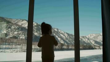 Sad child looks through the window while standing at home. video