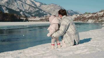 Mama und Kind sind Sitzung in der Nähe von das Fluss im Winter. video