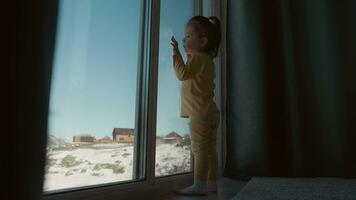 das Kind steht in der Nähe von das Fenster von das Haus und ist traurig. video