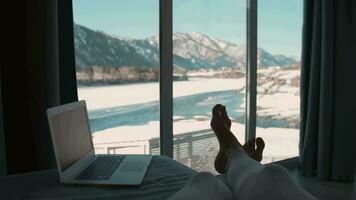 A female freelancer lies on a bed next to a laptop and looks out the window while on vacation. video