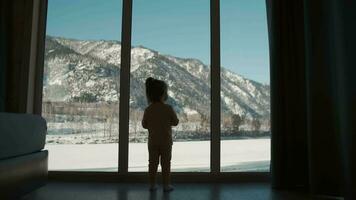 2 year old child stands at the window and looks outside at home video