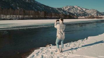 femme blogueur voyageur prend une photo en utilisant une téléphone intelligent tandis que permanent dans le montagnes près le rivière. video