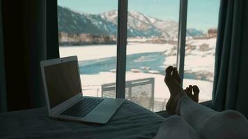 A woman lies on a bed next to a laptop and looks out the window. video