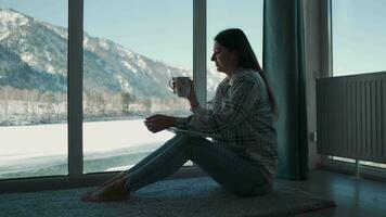 A woman sits near the window and drinks tea from a mug. video