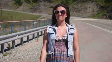 retrato. un hermosa niña camina a lo largo el la carretera y vueltas a Mira a el hermosa ver de el montañas y bosque video