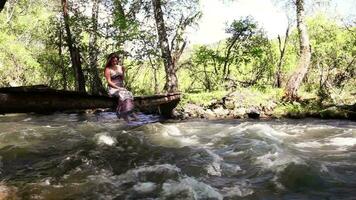 A beautiful girl is sitting on the bridge playing with her legs. There is a river under the bridge video