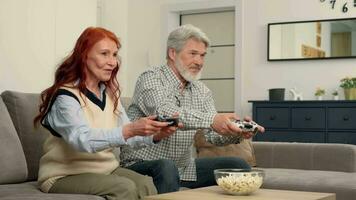 vrolijk senior paar 50-60 jaren oud spelen een video spel Bij huis zittend Aan de bank.