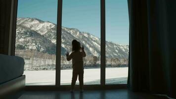 un pequeño niño soportes cerca el ventana y golpea en el ventana con su mano. video