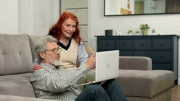 Happy senior couple aged 60-70 make an online purchase at home using a laptop. video