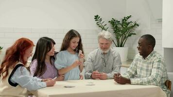 Multi ethnic family of different age generations play cards at home sitting at the table. The child wins. video