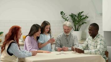 alegre multiétnico familia de diferente años generaciones jugando tarjetas a hogar sentado a el mesa en el cocina. video