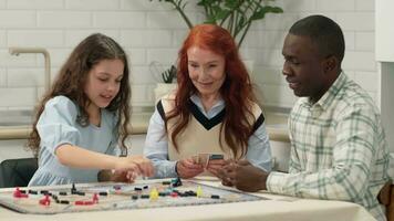 Multi Ethnic family of different age generations play board game at home sitting at the table. The child throws the dice on the table and makes a move. video