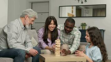 Multiethnic family of different age generations playing board game at home. Dad removes the wooden blocks from the tower and loses. video