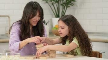 alegre mãe e alegre filha jogar uma borda jogos às casa às a mesa construção uma torre do de madeira blocos. video