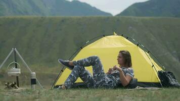 Mädchen Tourist ruhen Lügen im Vorderseite von das Zelt mit ein Becher von Tee im ihr Hände video