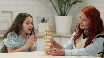 Grandmother and granddaughter are playing a board game at home removing wooden blocks from the tower. video