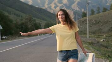 Beautiful girl tourist stops the car with the hand while walking on the highway with a map in hand video