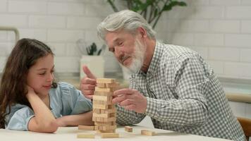 Grandfather and granddaughter are playing a board game at home removing wooden blocks from the tower. video