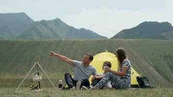 A happy family with a child is resting together in front of the tent and drinking tea from a thermos. video