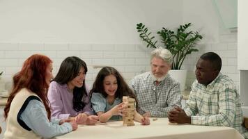 Cheerful multi ethnic family of different age generations playing board game at home. The daughter removes wooden blocks from the tower and the tower collapses. video