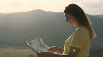 retrato. un hembra turista con largo pelo soportes en el borde de un acantilado con un mapa en su manos y es mirando para un ruta para viajar. video