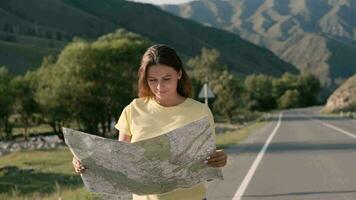 Attractive female tourist with a map in hands travels walking on the highway in a good mood video