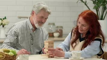 un' anziano coppia nel loro 60s e 70s giocare un' tavola gioco a casa rimozione di legno cubi a partire dal un' Torre. video