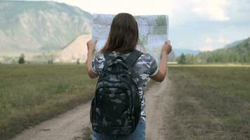 atractivo mujer turista va en el la carretera con un mapa en su manos en un antecedentes de montañas. espalda vista. video