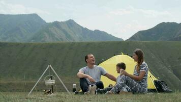 glücklich Familie mit ein Kind Lachen auf Campingplatz in der Nähe von ein Zelt mit ein Lagerfeuer. video