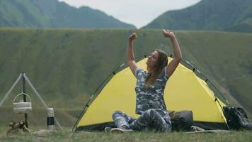 Girl tourist after sleep pulls his hands up sitting in front of a spider house in the mountains in sunny weather video