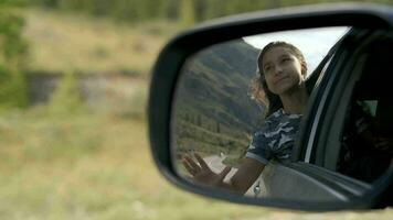 el niña relaja en un Moviente coche mientras sentado por el ventana. reflexión en un coche espejo. viaje. video