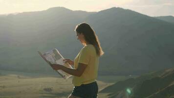 Camera movement around a tourist girl who stands on the edge of a cliff and holds a map in her hands video