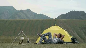 Girl tourist relaxes lying in front of the tent on a background of mountains in sunny weather video