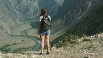 Female traveler with a rucksack stands on the edge of the mountain and rejoices at success raising his hands up video