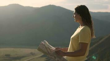 retrato. un hembra turista con largo pelo soportes en el borde de un acantilado con un mapa en su manos y mira dentro el distancia video