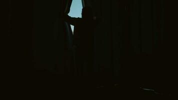 un' donna si apre il le tende con sua mani mentre in piedi a il finestra nel il Camera da letto. video