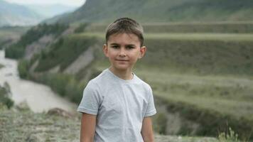 retrato. pequeño chico turista mirando a el cámara en un antecedentes de montañas y un río video