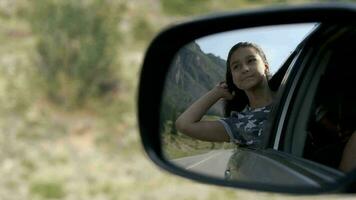 el niña relaja en un Moviente coche mientras sentado por el ventana en contra el fondo de el montañas. reflexión en un coche espejo. viaje. video