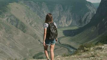 un hembra viajero con un mochila sube a el parte superior de el montaña y levanta su manos arriba, sensación un sentido de buceo y éxito. espalda ver video