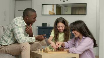 Happy family of three people of different races play chess at home in the living room. video