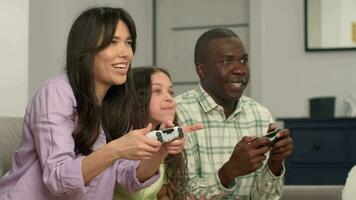 Multi ethnic family playing video game at home sitting on sofa.