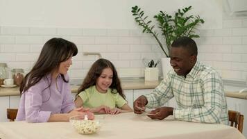 Multi ethnic family of three play cards at home sitting at the table. video